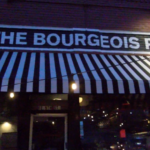 The sign and striped awning of the Bourgeois Pig, a cocktail bar on Massachusetts Street.