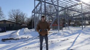 A KUJH reporter stands in the snow outside the steel structure of the new KU Chabad Center.