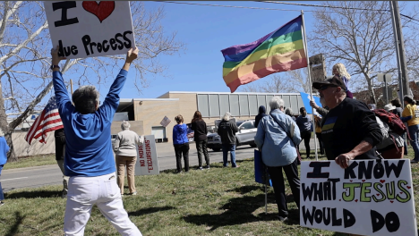 protesters hold signs and flags at a protest