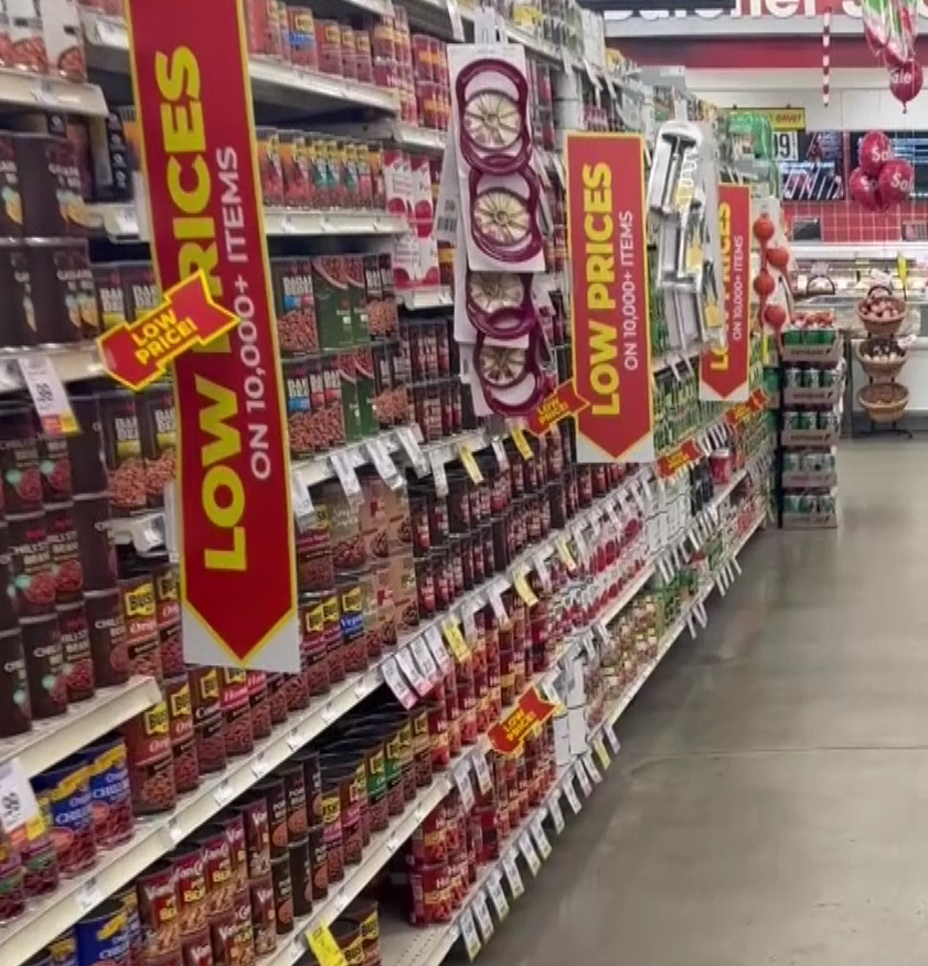 shelves lined with products at a grocery store, signs stick out from the shelves reading "Low prices"