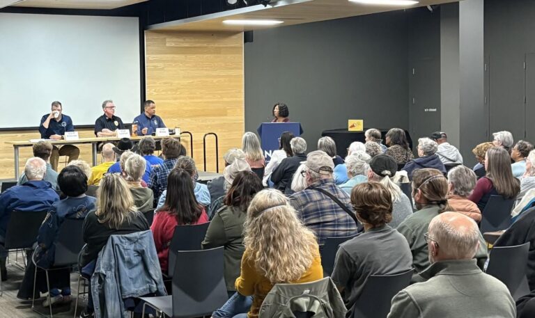 An audience of people faces a panel of speakers inside Lawrence Public Library