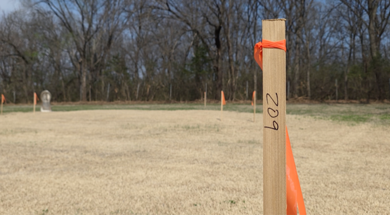 A wooden grave marker tied with an orange ribbon on top
